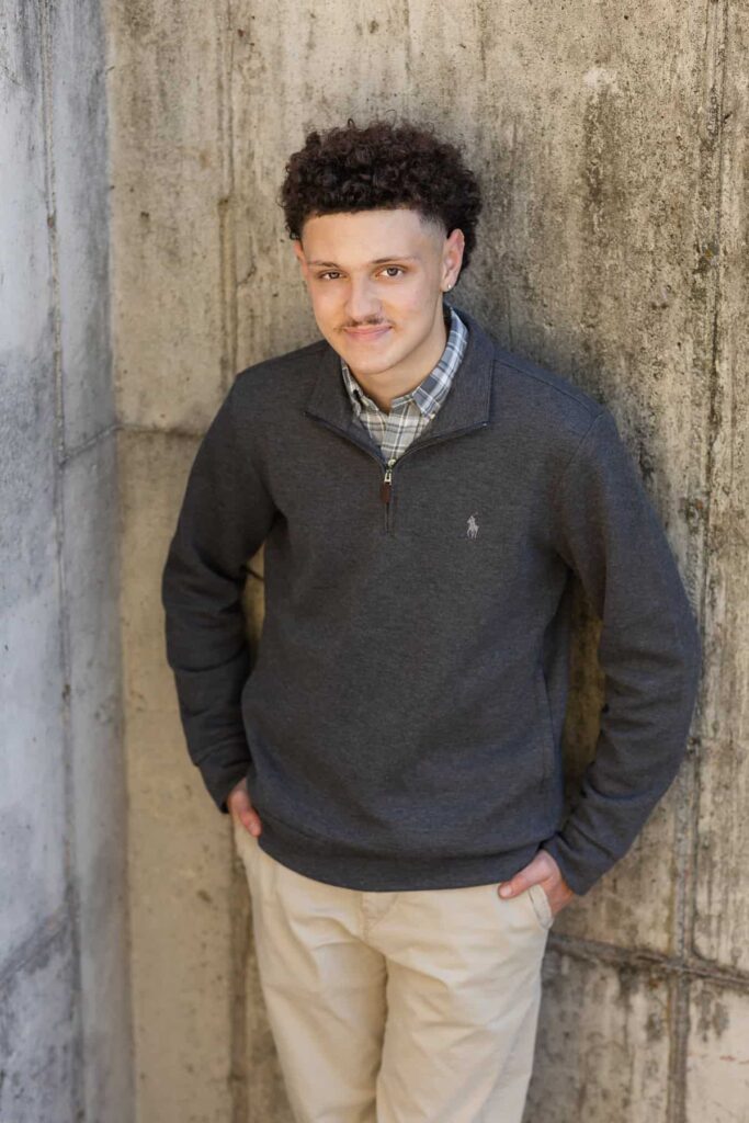 high school senior boy leaning on a cement wall looking at the camera